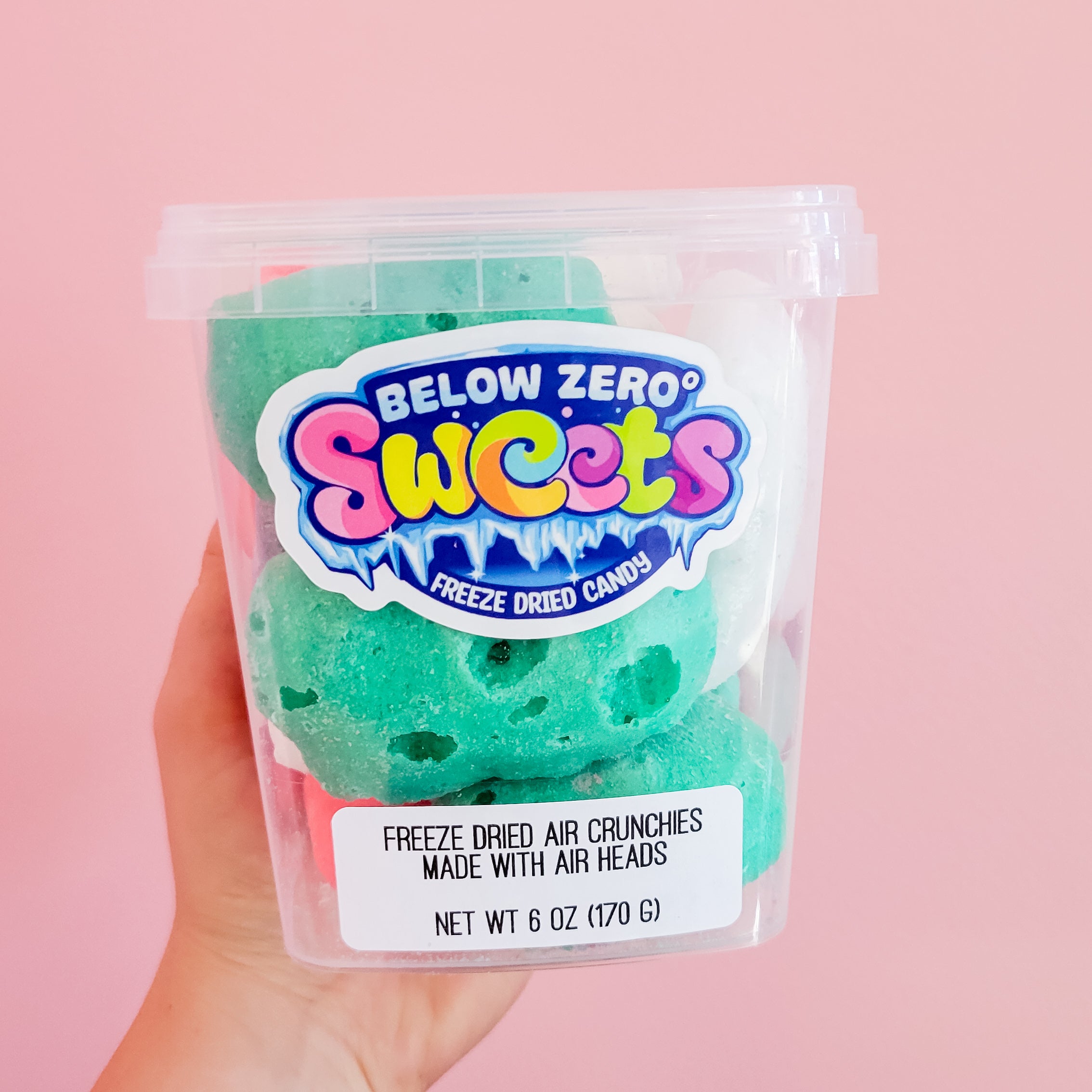 Freeze Dried Air Crunchies in a clear Below Zero Sweets tub held by a hand against a pink backdrop