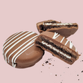 Four chocolate dipped Oreos with white drizzle on a pink background, one broken to show cream filling.
