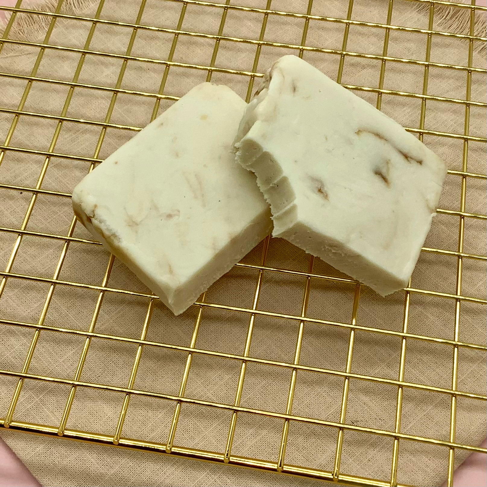 Two white Biscoff cheesecake fudge bars on a gold cooling rack