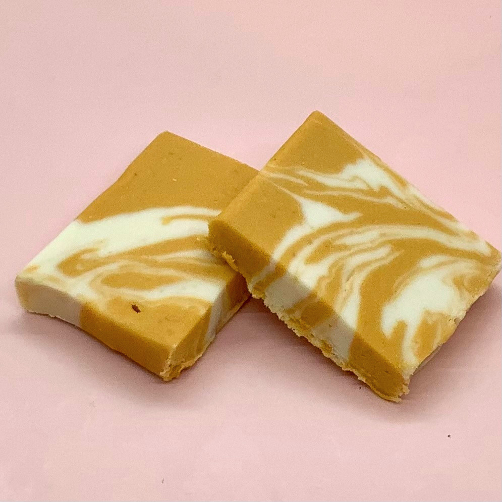 Two square pieces of butter beer fudge with caramel and white swirls on a pink background.