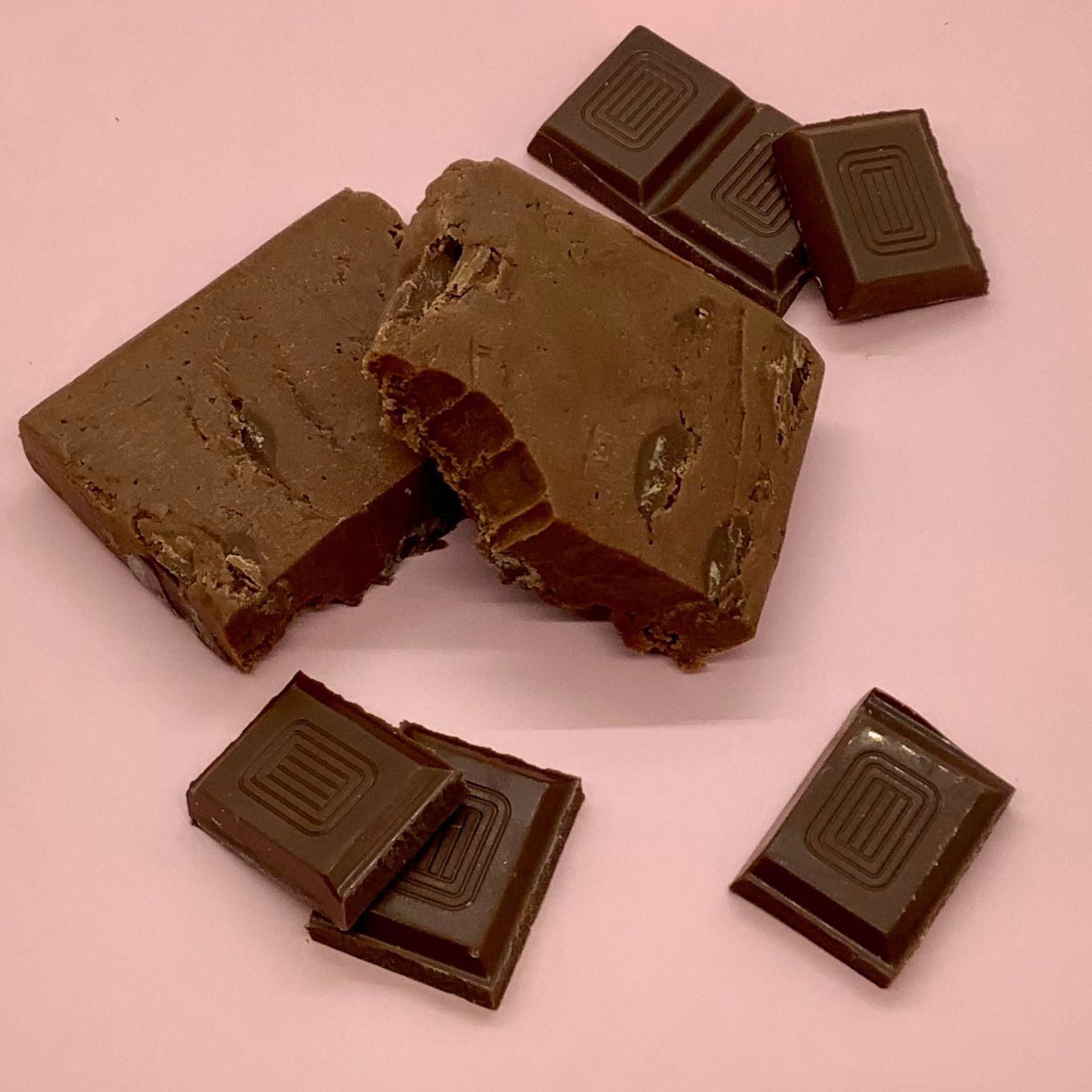Large slab of chocolate fudge with chunks and decorative dark chocolate squares scattered nearby.