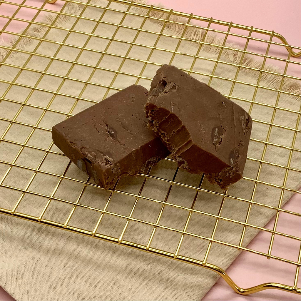 Two rectangular pieces of chocolate chunk fudge on a gold cooling rack.