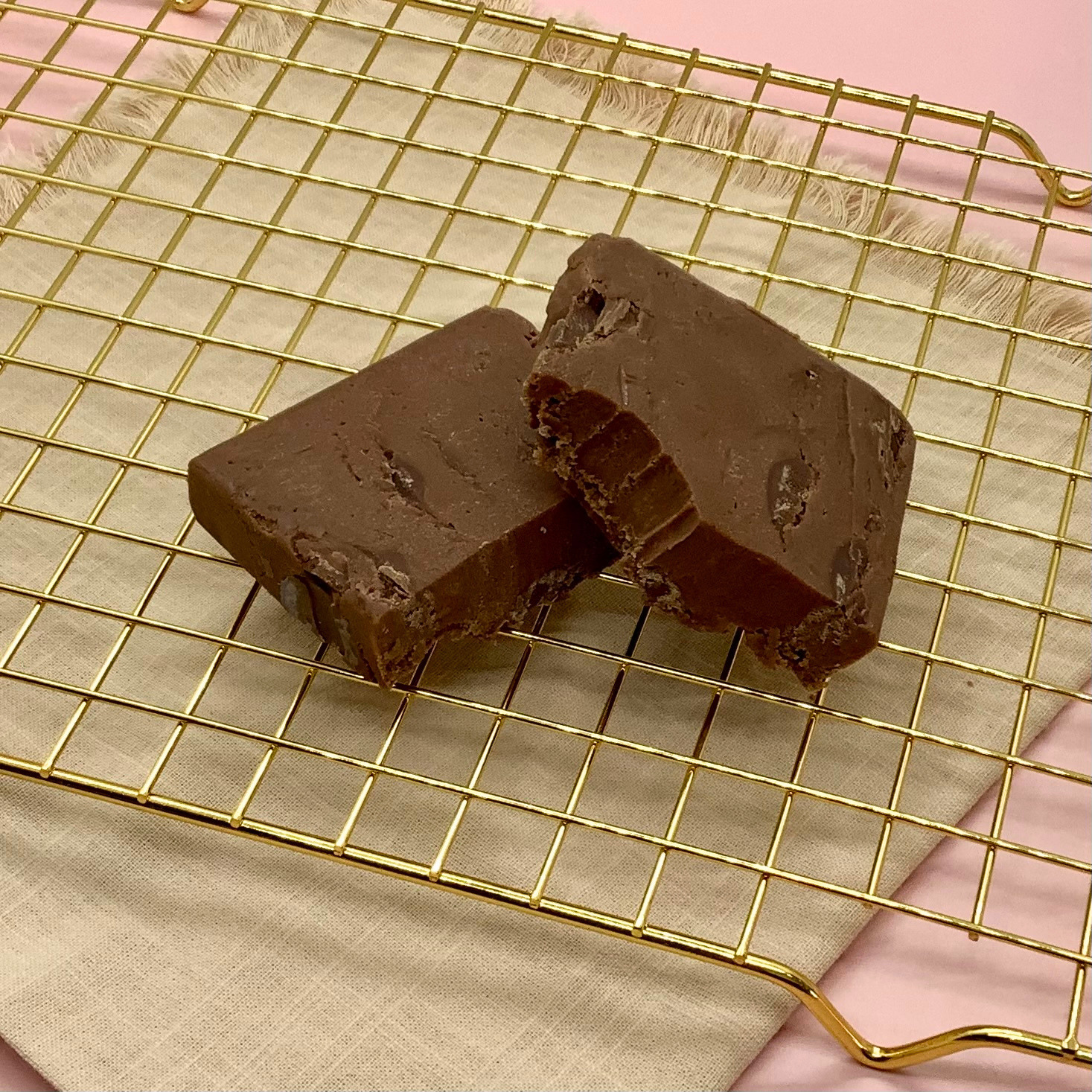 Two rectangular pieces of chocolate chunk fudge on a gold cooling rack.