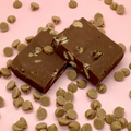 Chocolate peanut butter fudge squares with peanut pieces on a pink backdrop