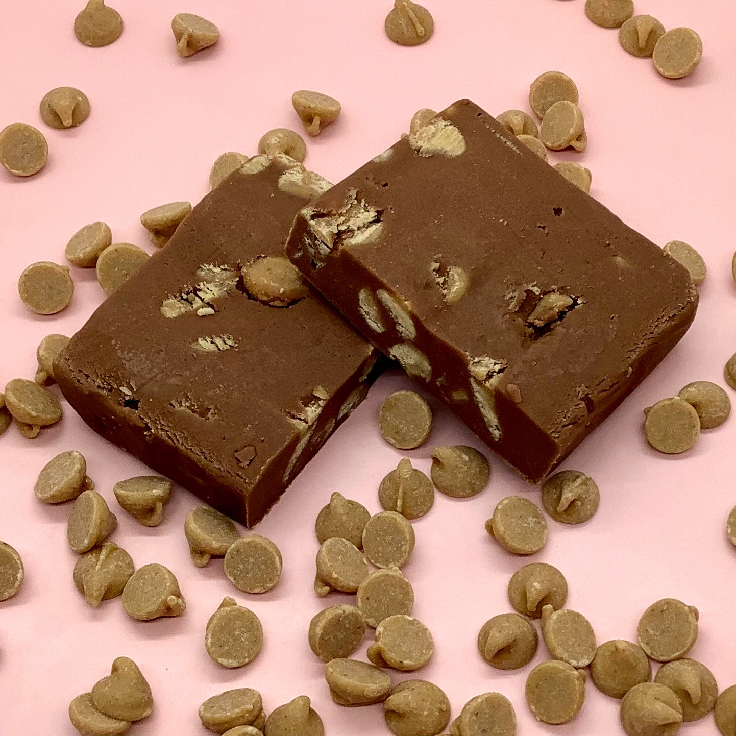 Chocolate peanut butter fudge squares with peanut pieces on a pink backdrop