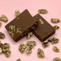 Two chocolate walnut fudge squares with visible walnut pieces on a pink background