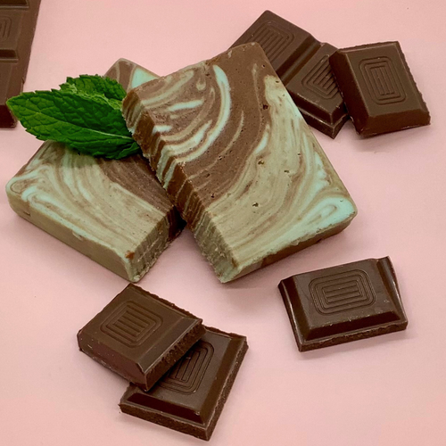 Swirled chocolate mint fudge blocks with mint leaves and pieces of dark chocolate on a pink background.
