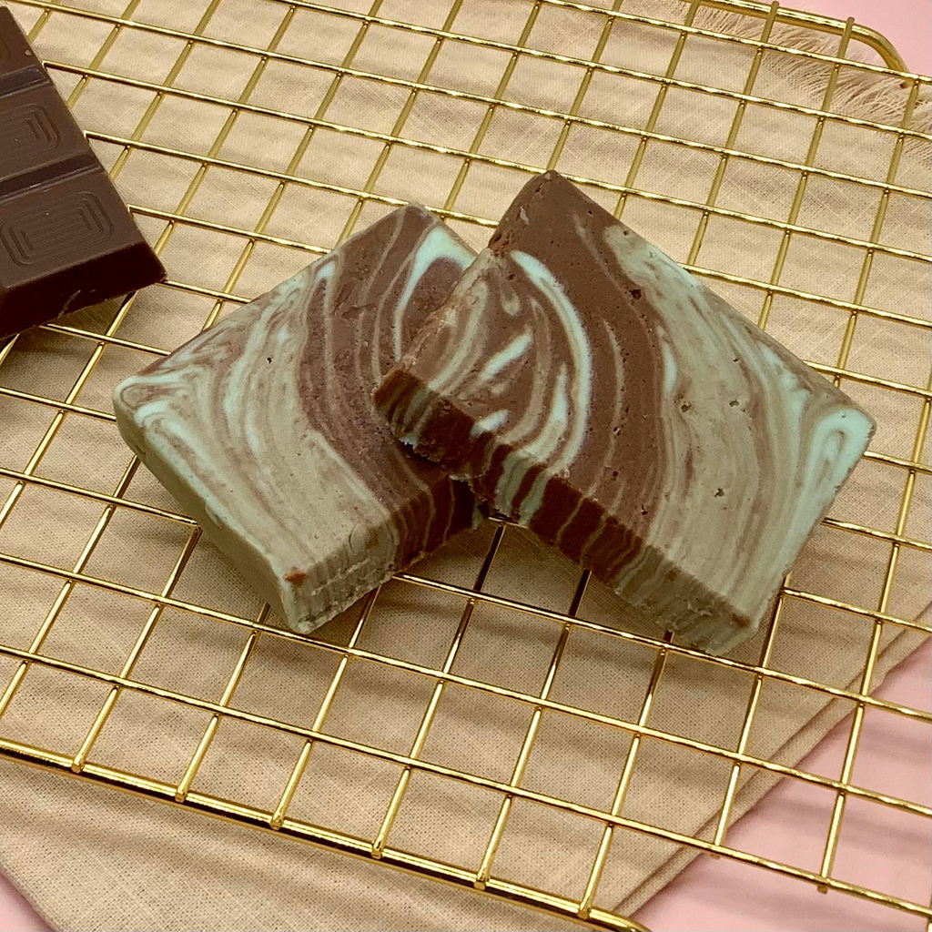 Marbled chocolate mint fudge slices on a gold cooling rack beside a dark chocolate bar.