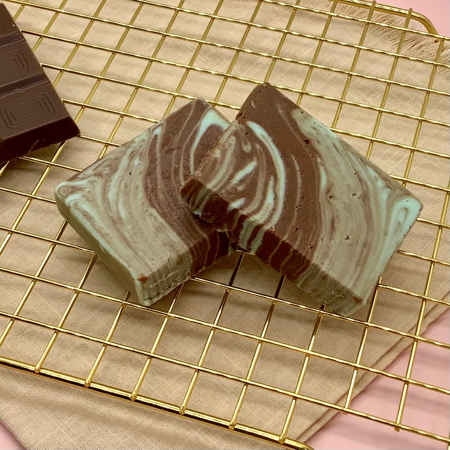Marbled chocolate mint fudge slices on a gold cooling rack beside a dark chocolate bar.