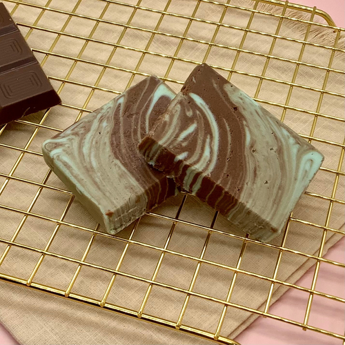Marbled chocolate mint fudge slices on a gold cooling rack beside a dark chocolate bar.