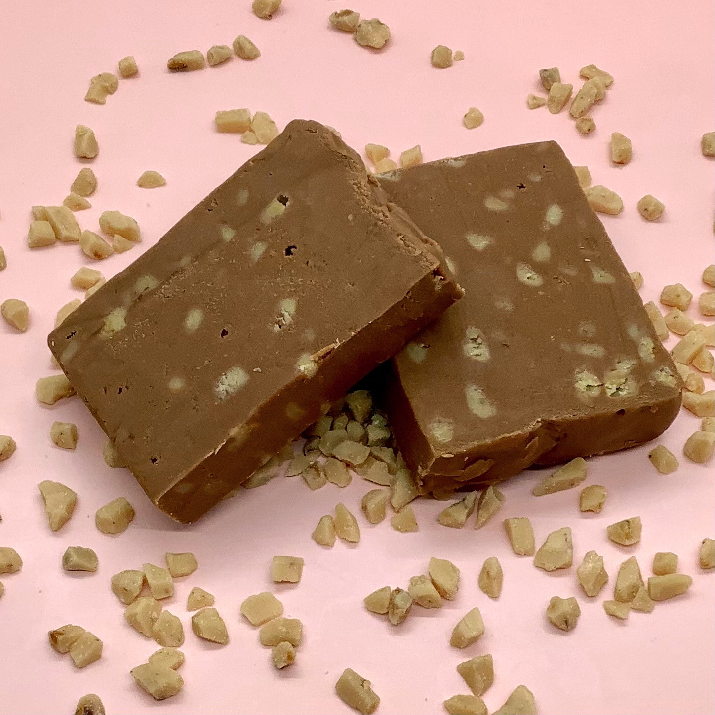 Two squares of English toffee fudge with white toffee chips on a pink backdrop.