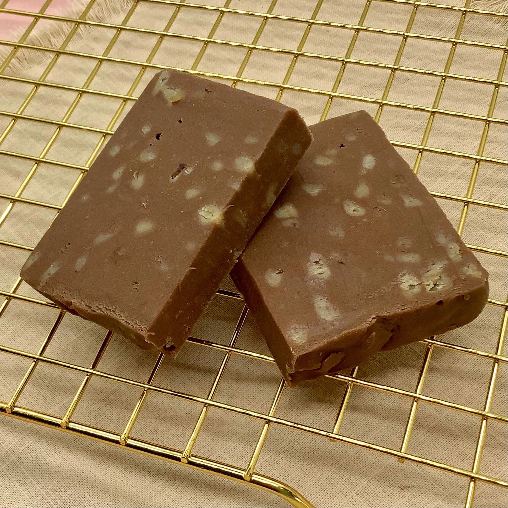 Two English toffee fudge blocks with white toffee bits on a beige surface.