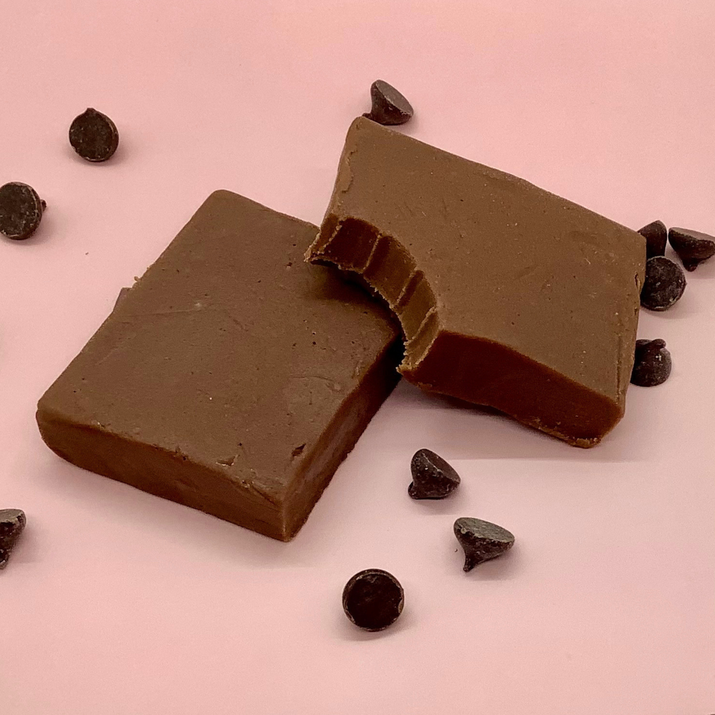 Two slabs of milk chocolate fudge on a pink surface with scattered dark chocolate chips