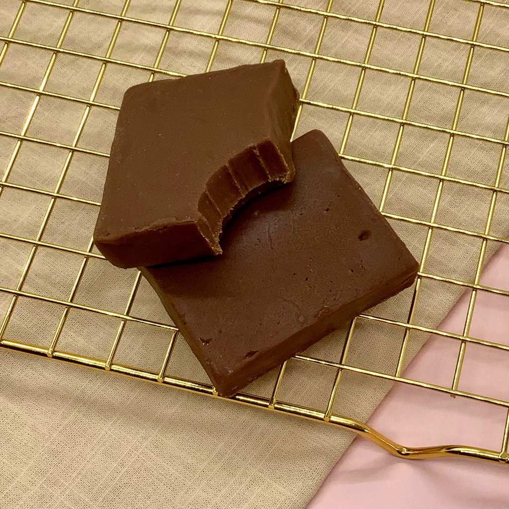 Two squares of milk chocolate fudge on a gold cooling rack with a bite taken from one piece