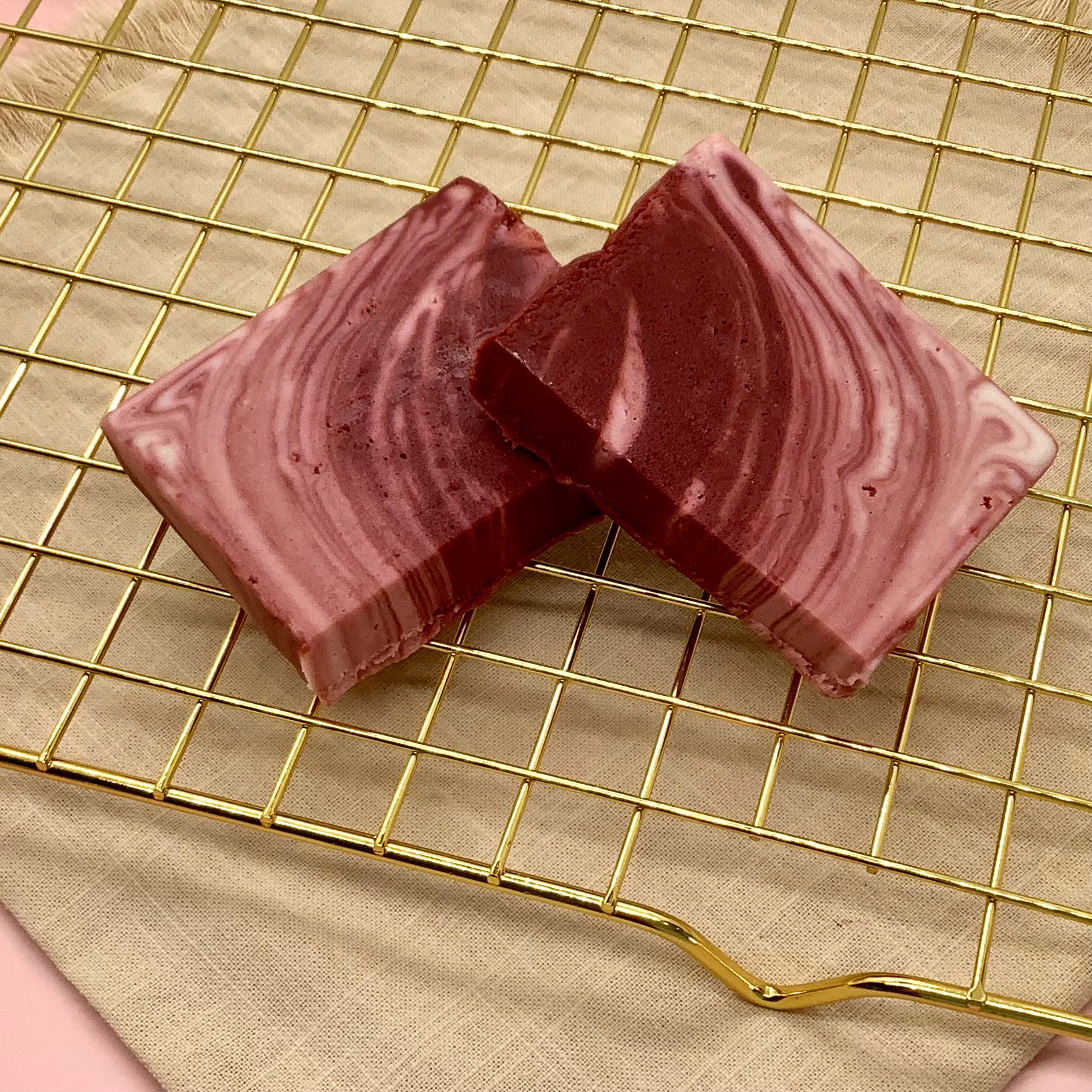 Marbled red velvet cheesecake fudge cut in half on a gold cooling rack with a pink background