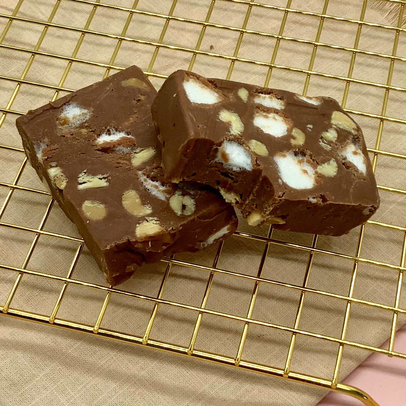 Rocky Road fudge squares with marshmallows and nuts on a gold cooling rack.