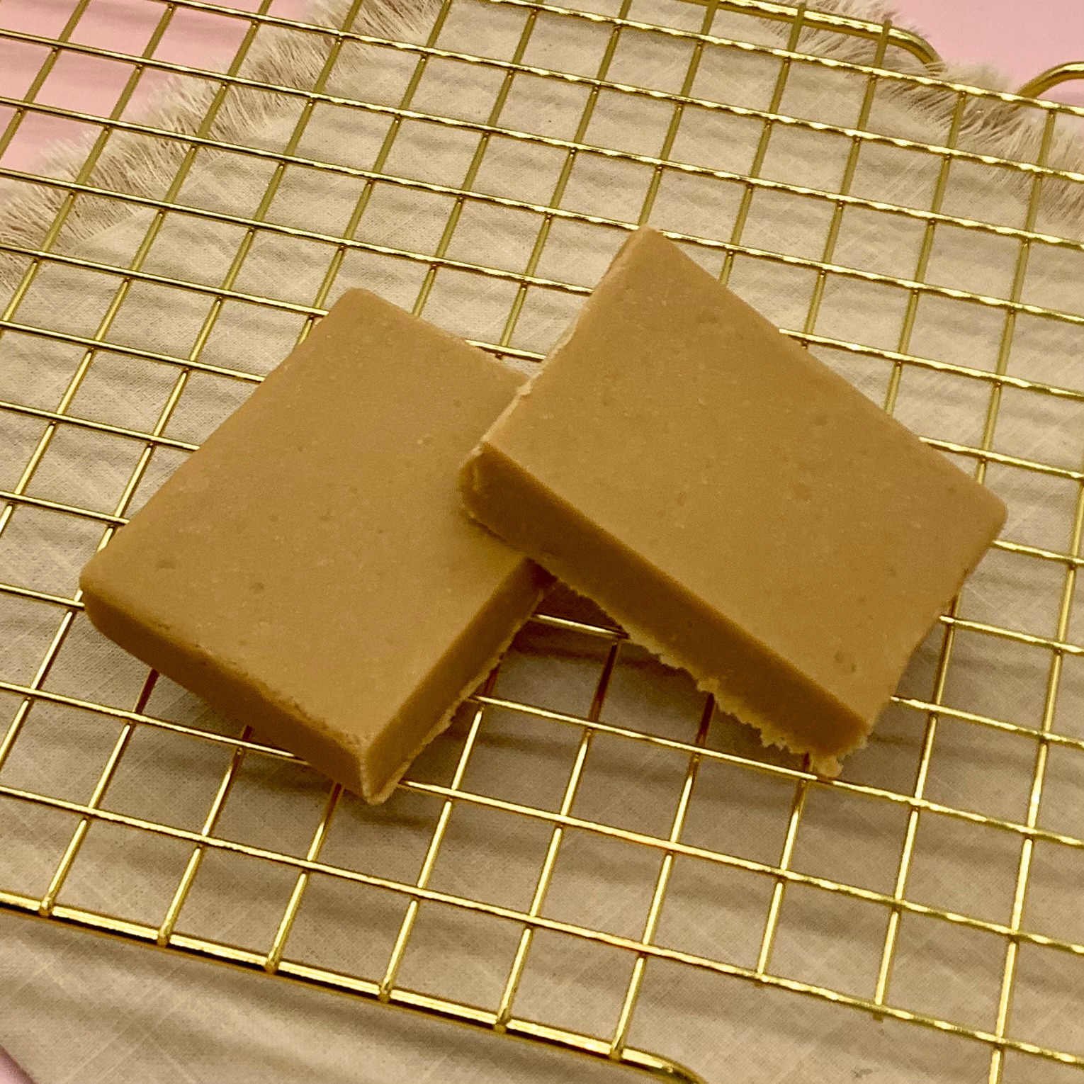 Salted caramel fudge squares on a gold cooling rack over beige fabric