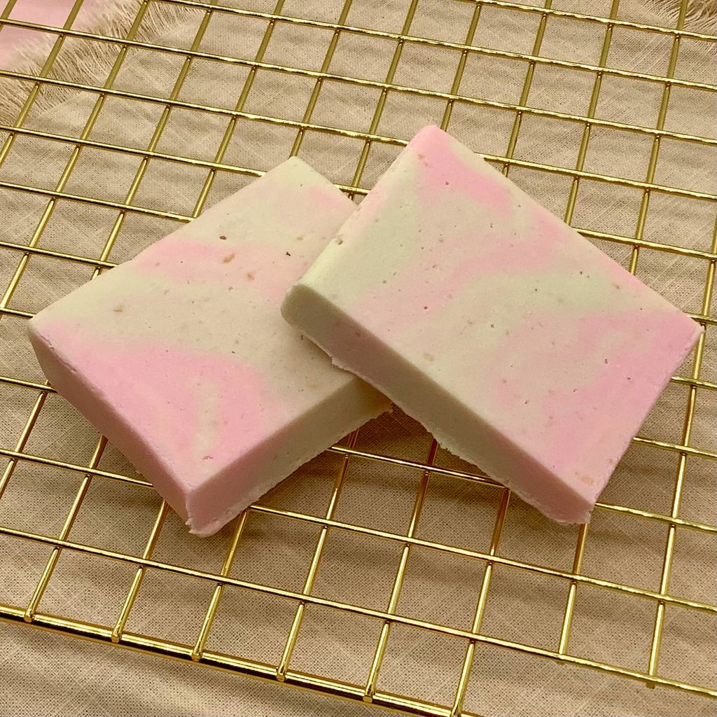 Strawberry cheesecake fudge swirls in pink and white, cut into squares on a gold cooling rack.